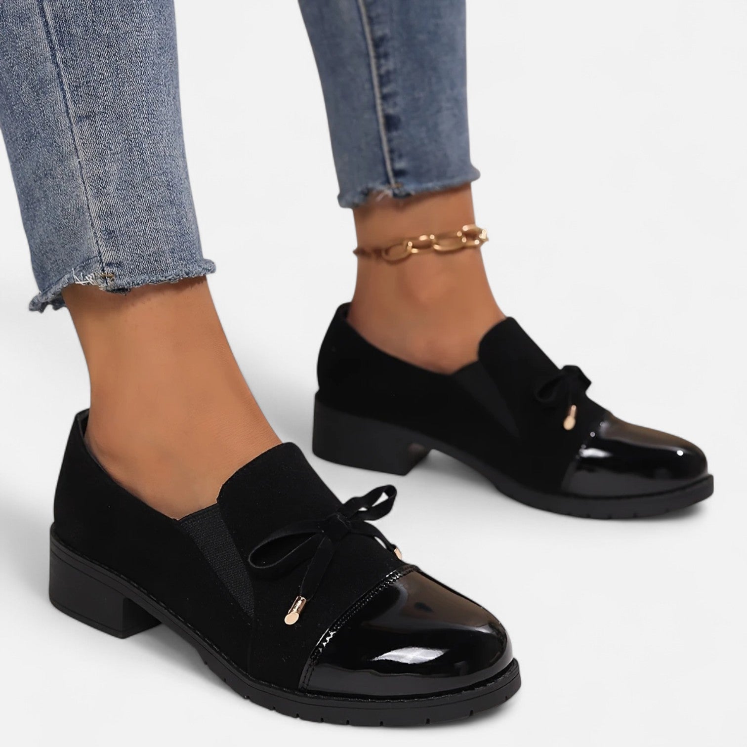 Black patent leather loafers worn with blue jeans on a light gray background