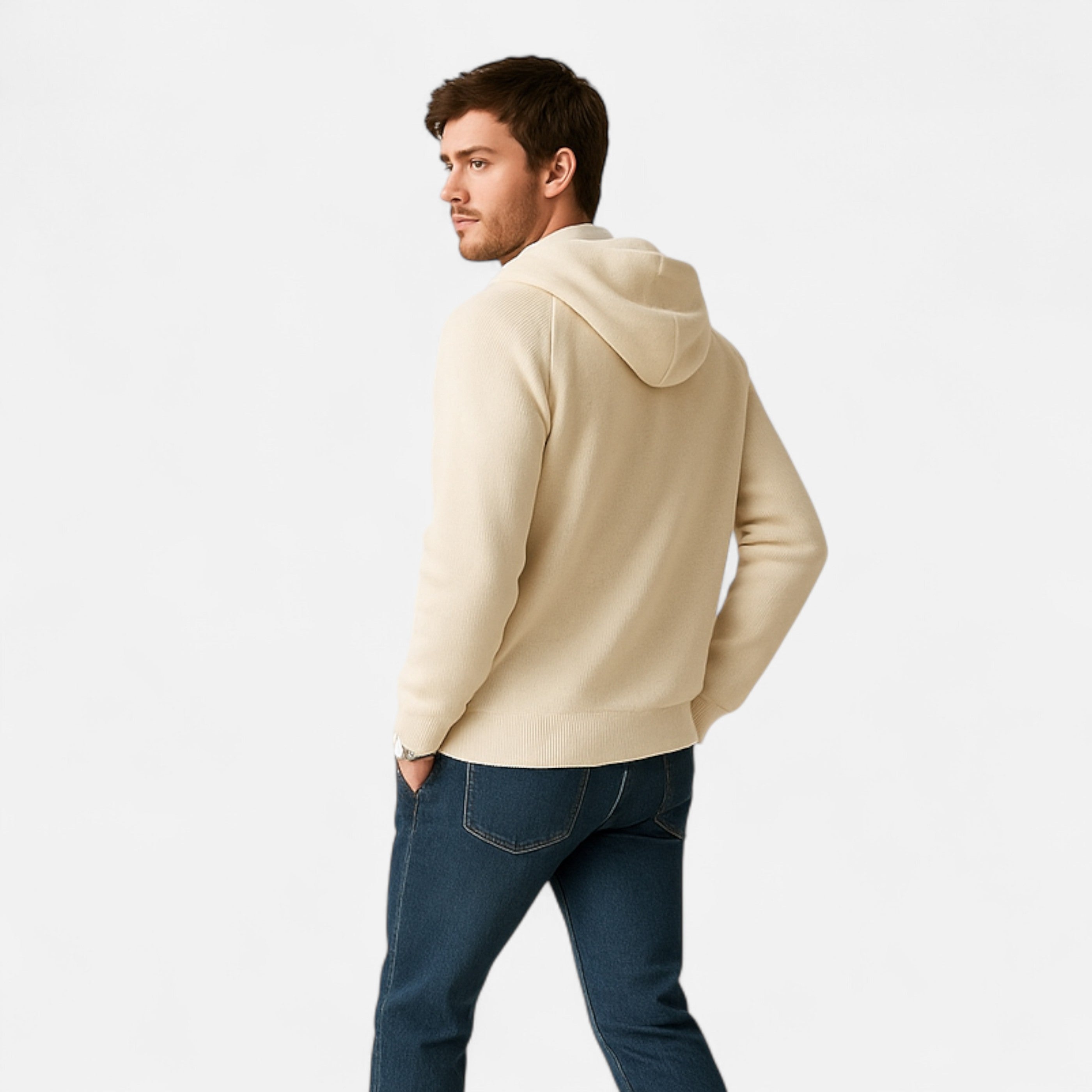 Man wearing a beige hoodie and blue jeans on a white background