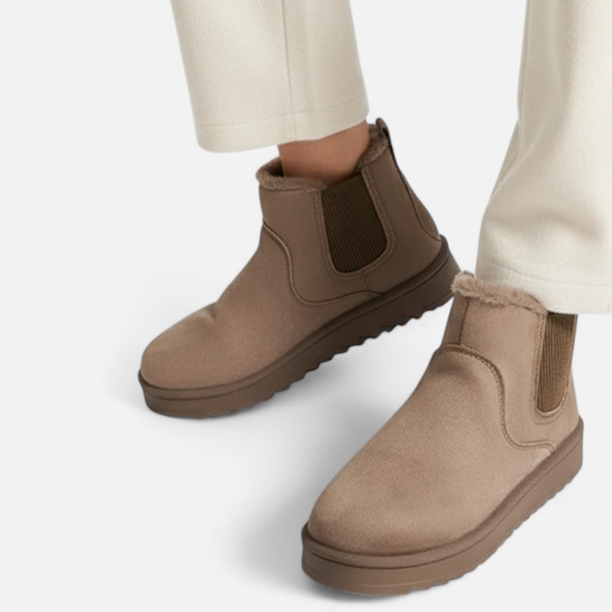 Brown suede ankle boots worn with beige pants on a white background