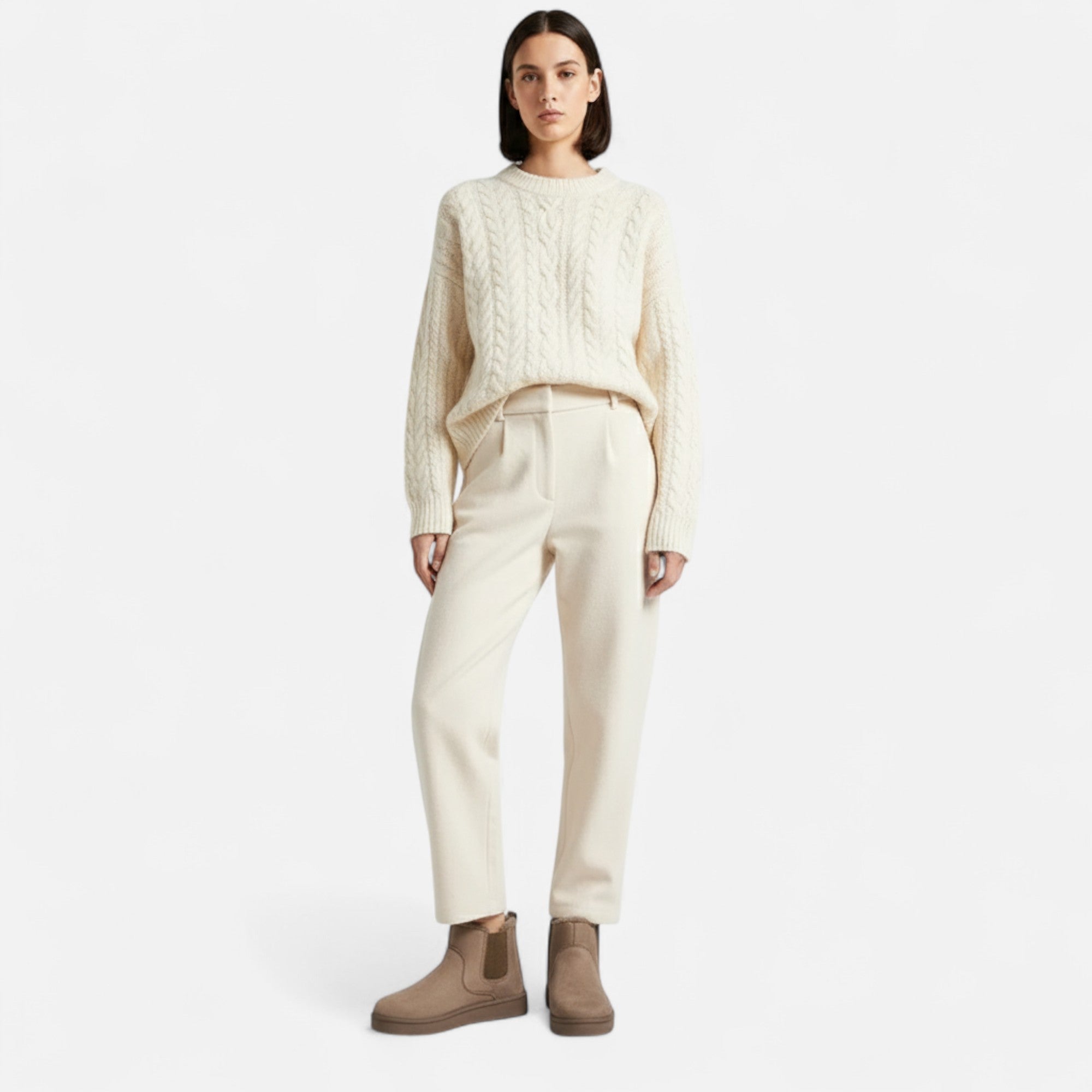 Person wearing a cream sweater and pants with brown boots on a white background