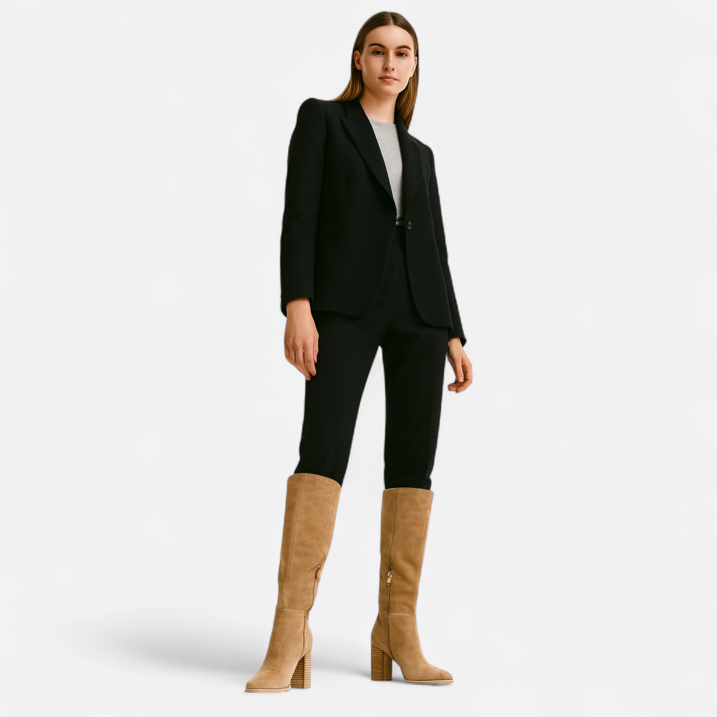 Woman wearing a black suit with tan knee-high boots on a white background